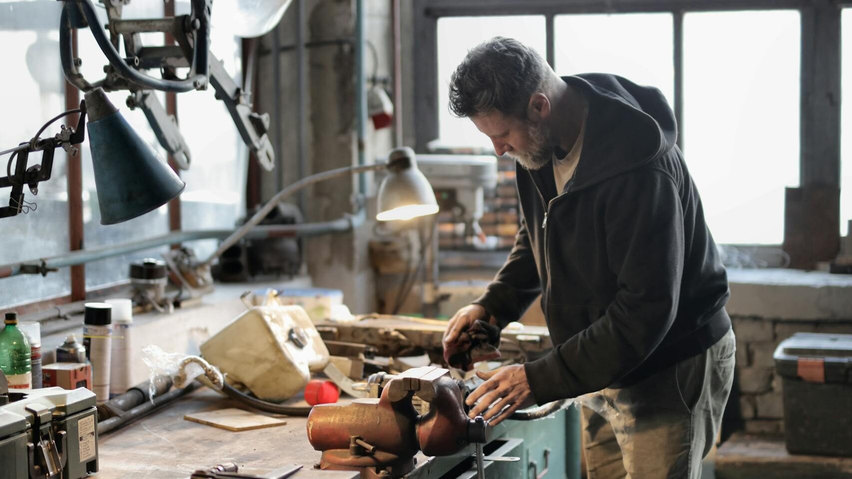 Side view of bearded male master in casual clothes standing at workbench and fixing details with professional metal instrument